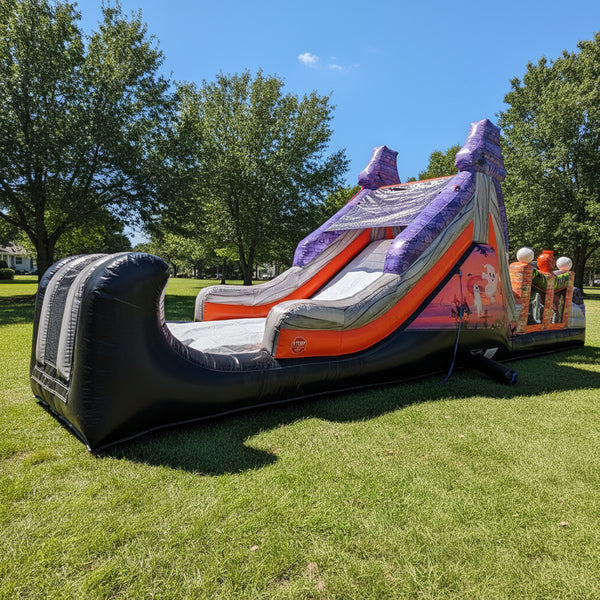 An inflatable bouncy castle slide with a pirate theme, featuring a black hull, orange side panels, a gray slide surface, and purple pirate hats at the top, isolated on a white background.