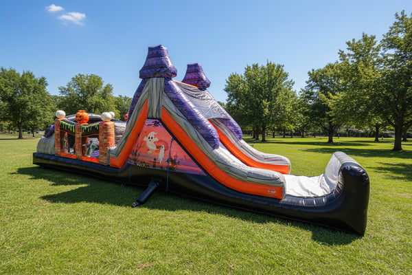 An inflatable Halloween-themed bounce house with a slide, featuring purple mountain peaks, orange and gray rock textures, a ghost graphic, and a black base, isolated on a white background.